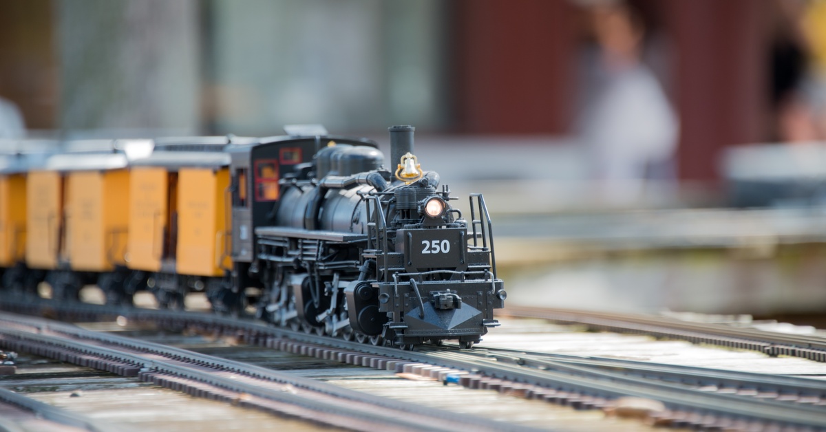 A model train display with multiple tracks. A black steam engine train leads several yellow cars behind it.